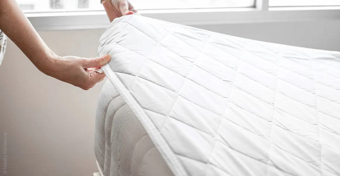 Photo: Two hands grasping a mattress protector lying on a mattress at one corner